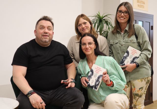 Na zdjęciu znajduje się Bartosz Węglarczyk oraz trzy kobiety robiące sobie z nim wspólne zdjęcie, dwie kobiety trzymają w ręce jego książkę. W tle znajduje się kwiat oraz drzwi.