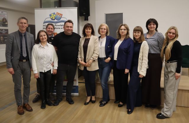 Na zdjęciu znajduje się osiem kobiet oraz dwóch mężczyzn stojących do wspólnego zdjęcia, za nimi znajduje się scena oraz baner z logiem biblioteki.