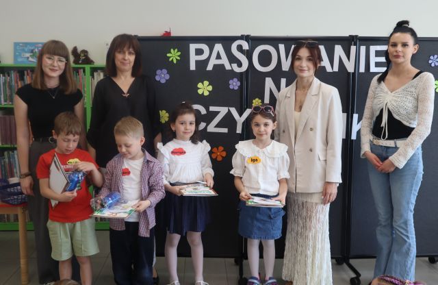 Na zdjęciu znajduje się czwórka dzieci z książkami, dyplomami, dwóch chłopców ma bidon, za nimi stoją cztery kobiety. W tle znajduje się czarna tablica z napisem i papierowymi kwiatami.