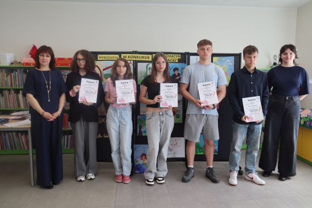 do zdjęcia pozuje 5 laureatów konkursu z książkami i dyplomami oraz dyrektorka biblioteki i bibliotekarka, w tle wystawa prac plastycznych