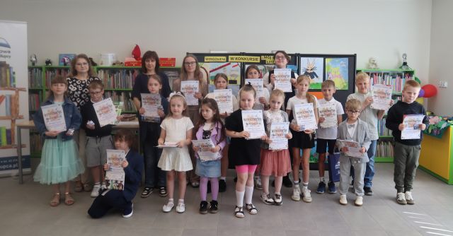 na zdjęciu 16 laureatów konkursu plastycznego z dyplomami i książkami oraz bibliotekarka i dyrektorka biblioteki