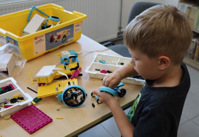Na zdjęciu znajduje się chłopiec, który buduje samochód z klocków LEGO przy stoliku.