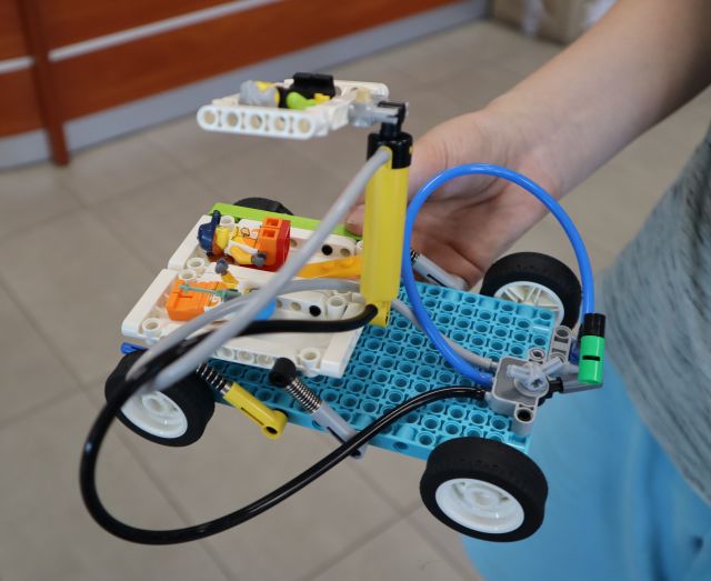 Na zdjęciu znajduje się zbudowana z klocków LEGO konstrukcja przypominająca łódkę, która jest trzymana w ręce przez chłopca. W tle znajduje się podłoga.
