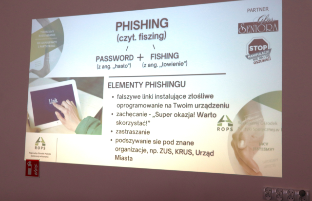 Na zdjęciu znajduje się wyświetlana na ścianie prezentacja przedstawiająca wyjaśnienie pojęcia phishingu.
