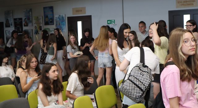 Na zdjęciu znajduje się młodzież stojąca w kolejce po zdjęcie i podpis, po lewej stronie znajdują się krzesełka, na których siedzi część młodzieży. W tle znajdują się plakaty powieszone na ścianach.