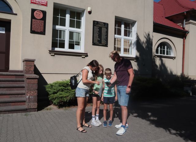Na zdjęciu znajduje się dwójka dzieci oraz kobieta z mężczyzną i rozwiązują zadanie z gry Wawrzynkowej przy Liceum Ogólnokształcącym.