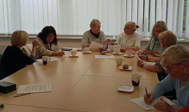na zdjęciu 8 seniorek, część rozmawia, część pisze na kartkach, część czyta z kartek