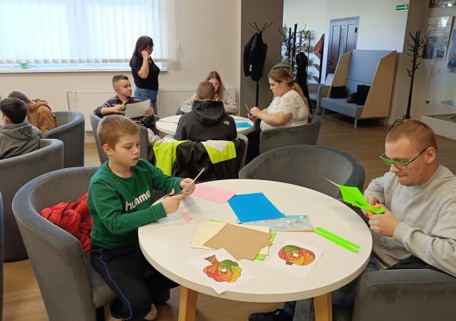 dzieci i młodzież wycinają z kolorowego papieru, siedzą przy okrągłych stołach