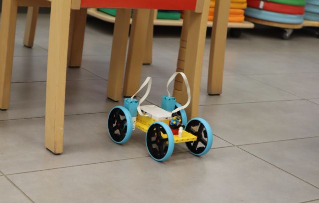 Na zdjęciu znajduje się zbudowany z klocków LEGO samochód jeżdżący na podłodze przy stolikach.