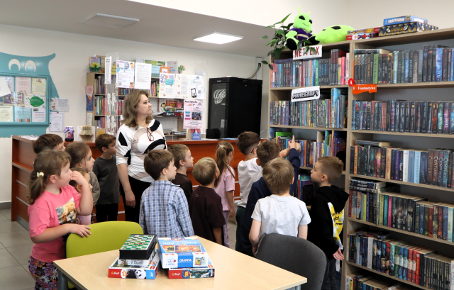 na zdjęciu przedszkolaki i bibliotekarka przed regałem z książkami, w tle biurko