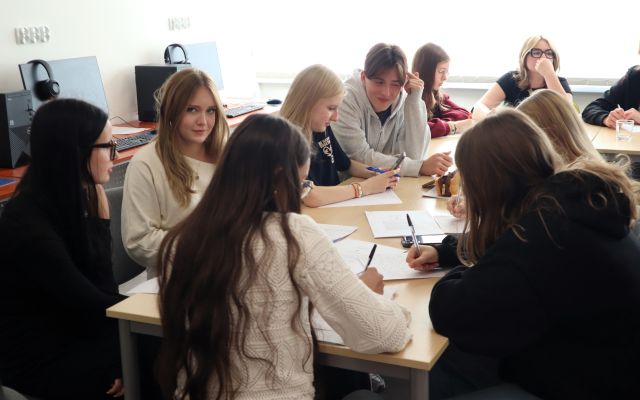 na zdjęciu młodzież siedząca przy stołach i robiąca notatki na kartkach