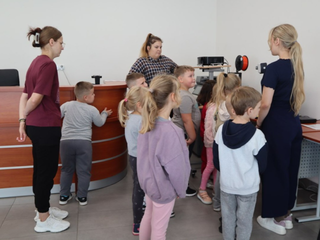 Na zdjęciu znajduje się grupka dzieci oraz trzy kobiety w sali komputerowej.