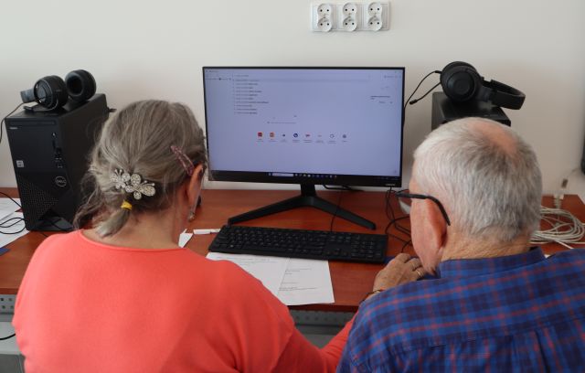 Na zdjęciu znajduje się kobieta i mężczyzna przy jednym komputerze, na którym odpalona jest przeglądarka internetowa. Zajęcia odbywają się w sali komputerowej.