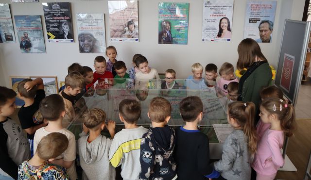 Na zdjęciu znajduje się 24 przedszkolaków oraz jedna kobieta dookoła makiety miasta. Na ścianie w tle znajdują się plakaty.