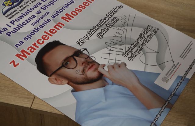 Na zdjęciu znajduje się leżący na podłodze plakat promujący spotkanie z Marcelem Mossem z autografem i wąsami na twarzy autora.