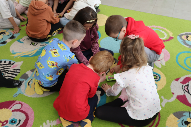 Na zdjęciu znajduje się 5 przedszkolaków, którzy wspólnie w grupie na dywanie układają puzzle związane z zawodami.