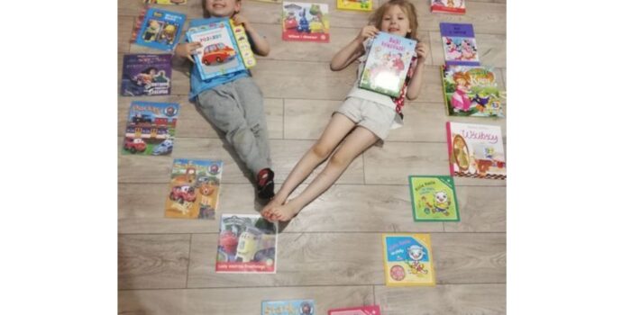 Dziewczynka i chłopiec leżą na podłodze tworząc serce. Wokół nich ułożone w serce książki