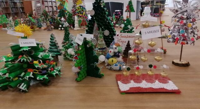 na brązowej podłodze 16 kolorowych choinek wykonanych z surowców wtórnych