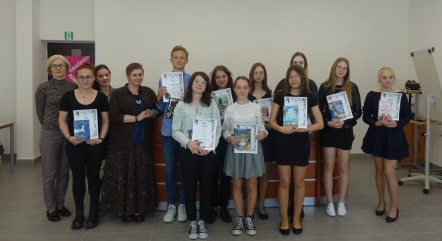 w dwóch rzędach stoją dziewczyny i chłopcy oraz dwie kobiety. Młodzież trzyma w rękach dyplomy i książki