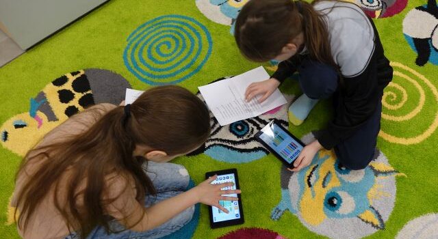 dwie dziewczynki za pomocą tabletów i zadania spisanego na kartce programują robota