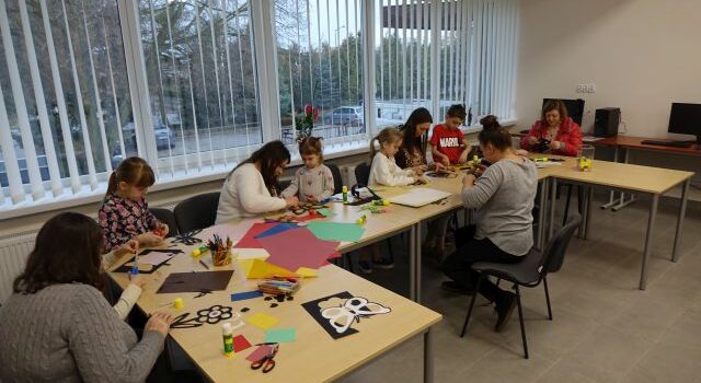 uczestnicy warsztatów dzieci i dorośli wykonują z papieru i kolorowej bibuły witraże
