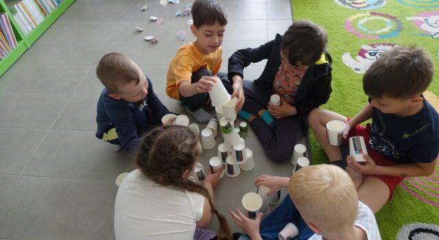 dzieci siedzą na podłodze i ukłądają plastikowe kubeczki