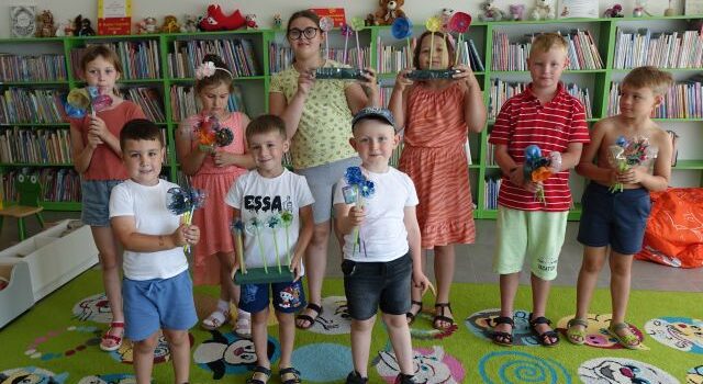 dzieci pozują do zdjęcia i pokazują wykonane przez siebie bukiety z plastikowych butelek, w tle regały z książkami