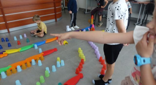 kolorowe kubeczki ułożone na podłodze w taki sposób że tworzą tor przeszkód dla robotó photon, dzieci sterują robotami używając tabletów