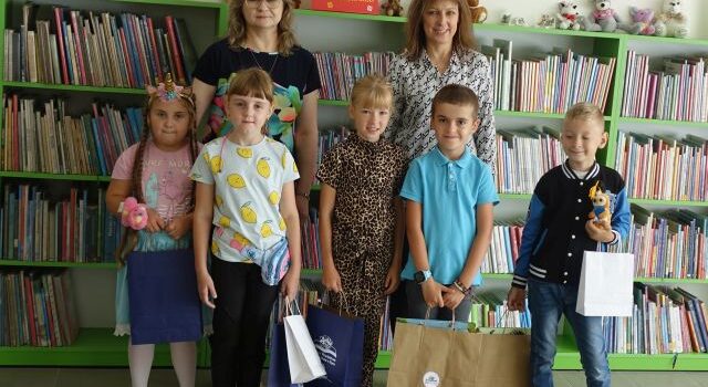 laureaci akcji bibliotecznej Paszport czytelniczy pozują z 2 bibliotekarkami i nagrodami do zdjęcia, w tle regały z książkami