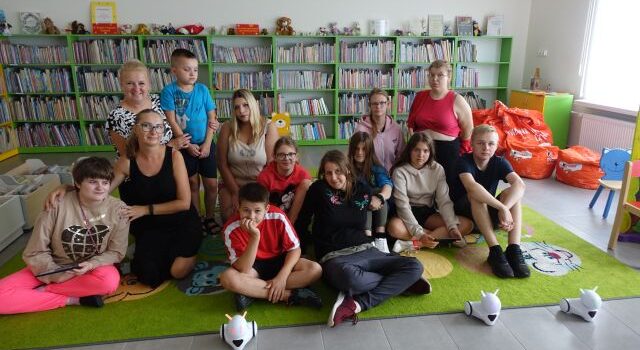 uczestnicy zajęć pozują do zdjęcia z robotami Photon, w tle regały z książkami