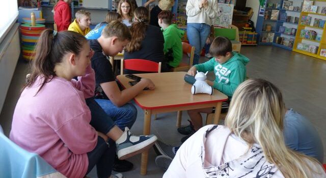 młodzież siedzi przy stolikach i steruje robotami Photon przy pomocy tabletów