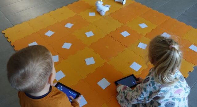 dzieci sterują przy użyciu tabletów robotami Photon jeżdżącymi po pomarańczowej macie
