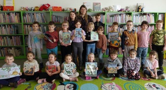 przedszkolaki i przedszkolanka pozują do zdjęcia trzymając w dłoniach książki o dinozaurach