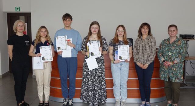 7 osób pozuje do zdjęcia, 4 osoby trzymają w dłoniach torebki z prezentami, książki i dyplomy