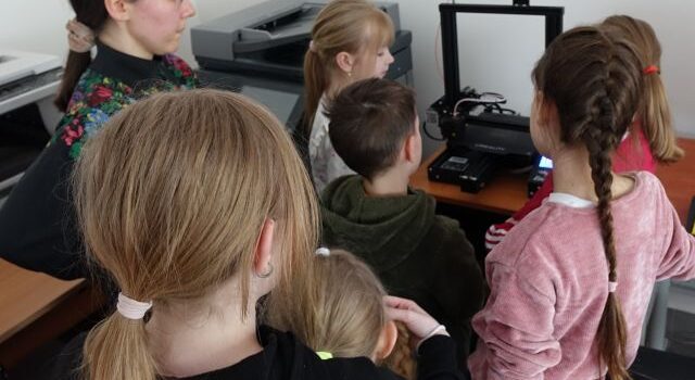 6 dzieci i biblioterka stoją przed drukarką 3d