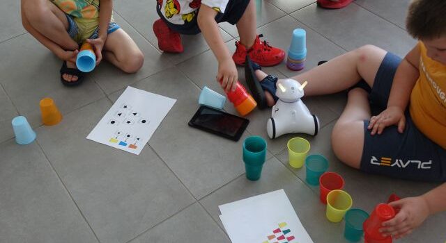 dzieci układają kolorowe kubeczki według wzoru rozrysowanego na kartkach