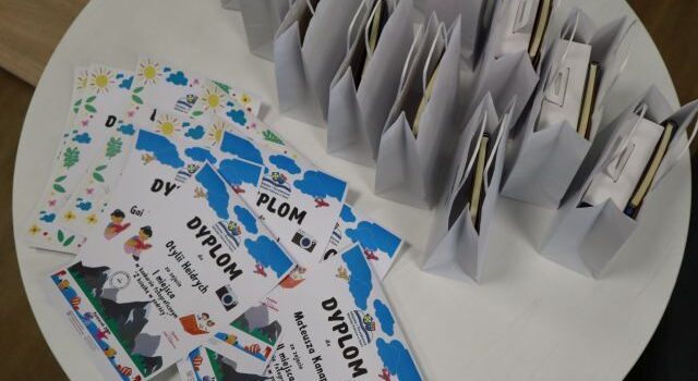 na białym okrągłym stole rozłożone dyplomy dla laureatów oraz nagrody w białych torebkach