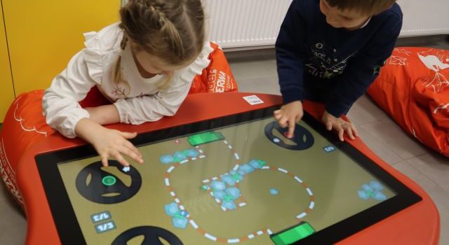 chłopiec i dziewczynka grają na stoliku interaktywnym
