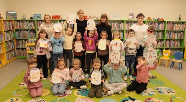 przedszkolaki pozują do zdjęcia ze swoimi pracami plastycznymi, nauczycielkami i bibliotekarką