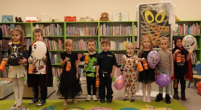 dzieci pozują do zdjęcia z wykonanymi przez siebie dyniami z papieru i balonami, w tle regały z książkami