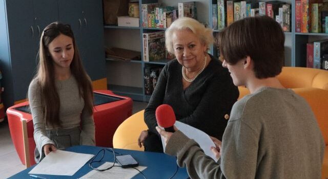 chłopak mówi do mikrofonu, przed nim siedzi kobieta i dziewczyna