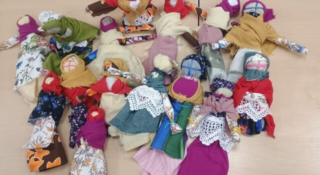 Na zdjęciu znajduje się piętnaście wykonanych na zajęciach motanych lalek leżących na stole.