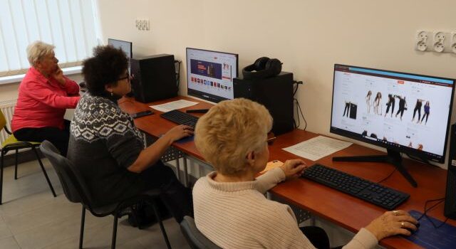 Na zdjęciu znajdują się trzy kobiety przy komputerach i przeglądają sklepy internetowe. Warsztaty odbywają się w sali komputerowej.