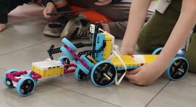 Na zdjęciu znajdują się dwa roboty z LEGO, robot po prawej jest zdecydowanie większy i jest trzymany rękoma.